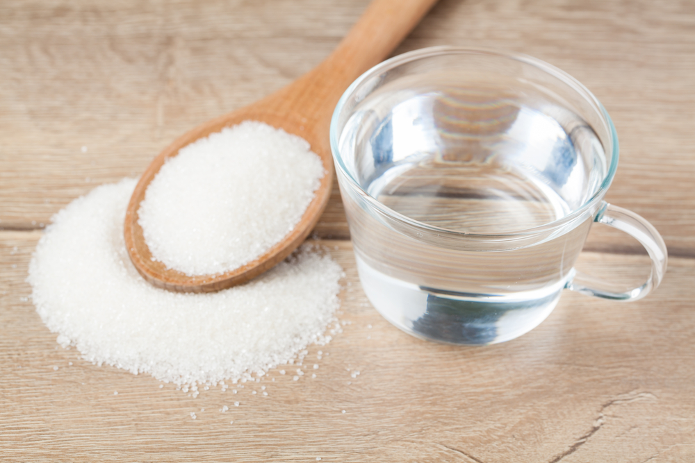 A wooden spoon with sugar next to a glass of water.