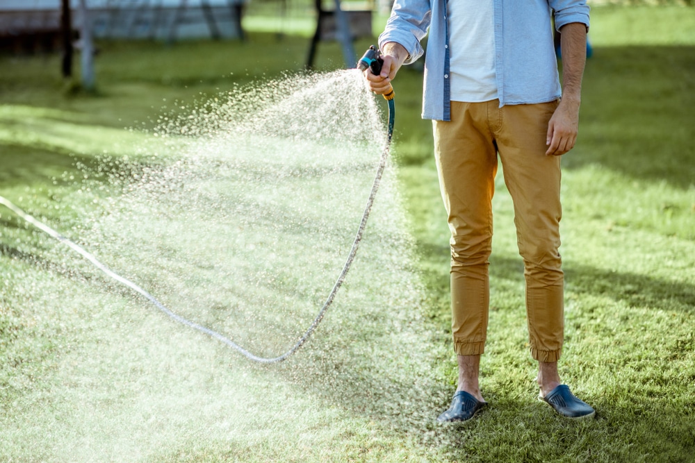 A man watering his lawn with a hose attachment.