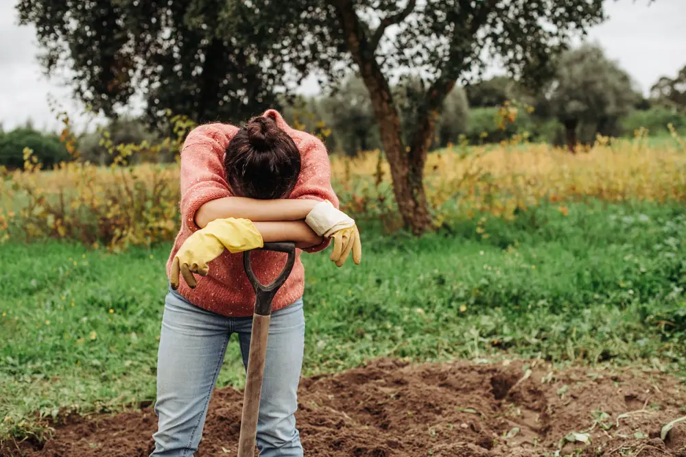 A tired female gardener leaning on a shovel.