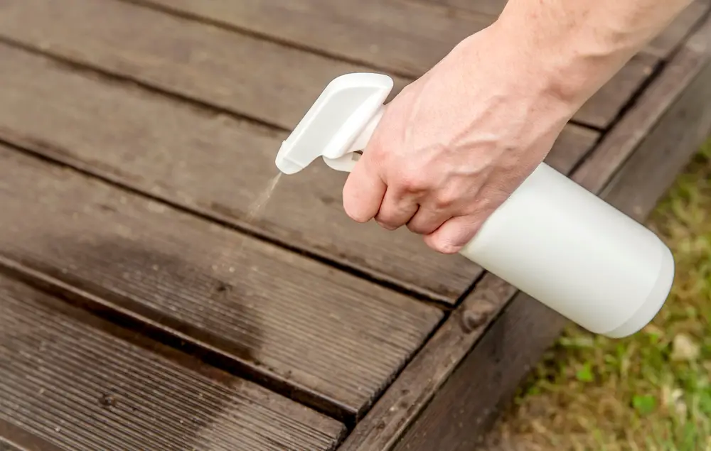 A person spraying their deck with insect repellent.