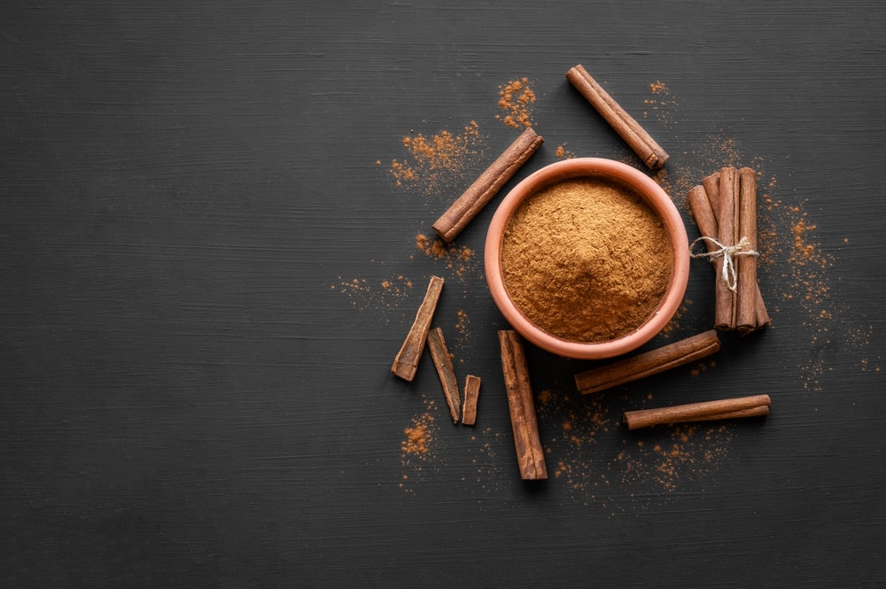 An overhead of ground cinnamon and cinnamon sticks on a black background.