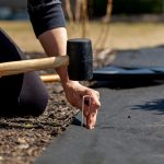 A person hammering a garden staple through landscape fabric.