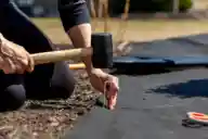 A person hammering a garden staple through landscape fabric.