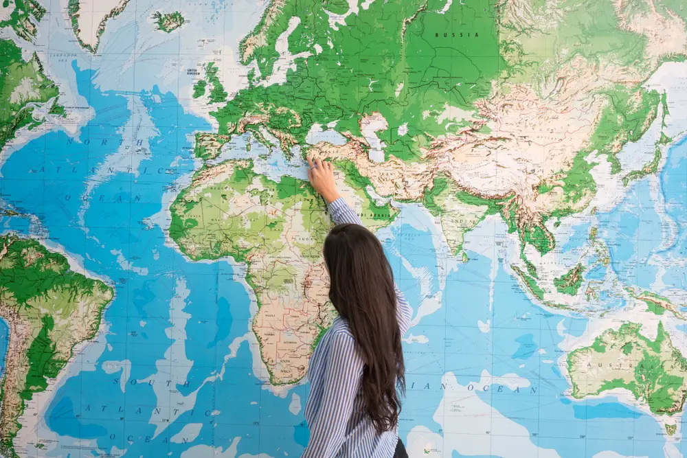 A woman from behind pointing at a world map.