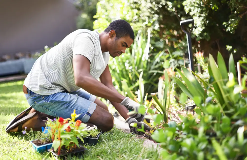 A man kneeling in the grass and digging in his garden to plant some things.
