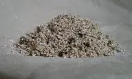 A small mound of coarse gray and beige sand on a plain surface, with individual grains visible around the edges.