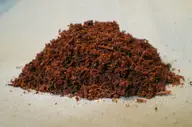 A mound of reddish-brown coconut coir on a pale surface, showing fine fibers and small clumps in the loose substrate.