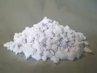 A mound of white horticultural perlite pieces on a gray surface, showing the irregular granules used in potting mixes.